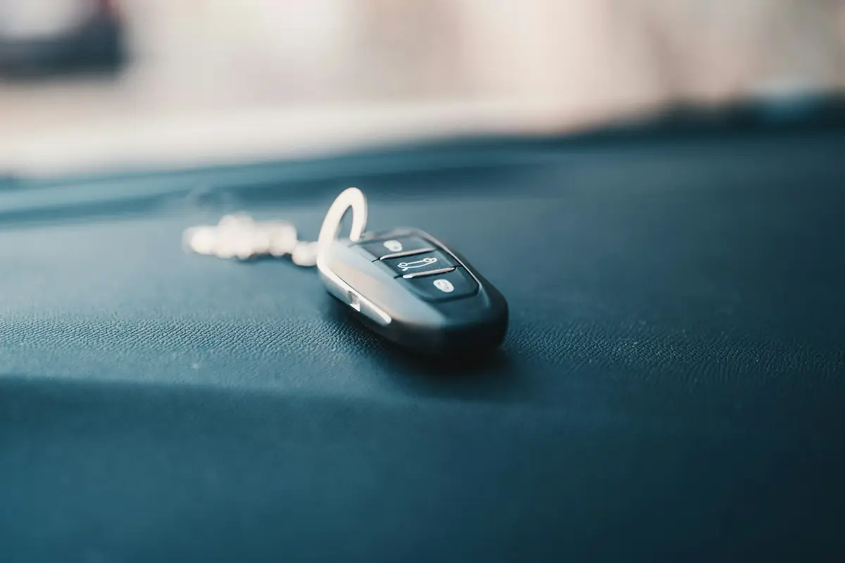 A gray and black car key fob on a ring, lying on a dark teal surface