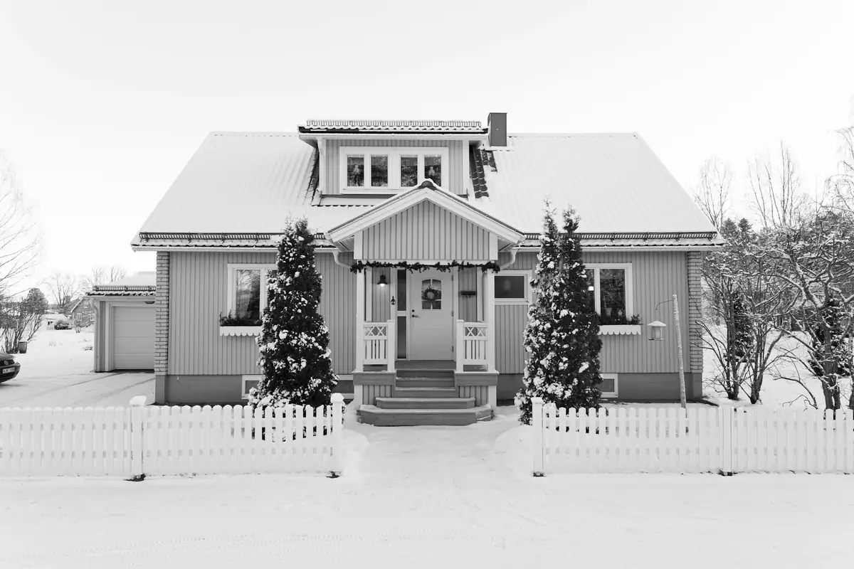A snow-covered house behind a white picket fence